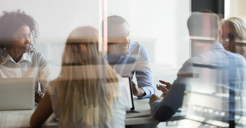 Diverse group of colleagues talking around a table with laptops in a modern office