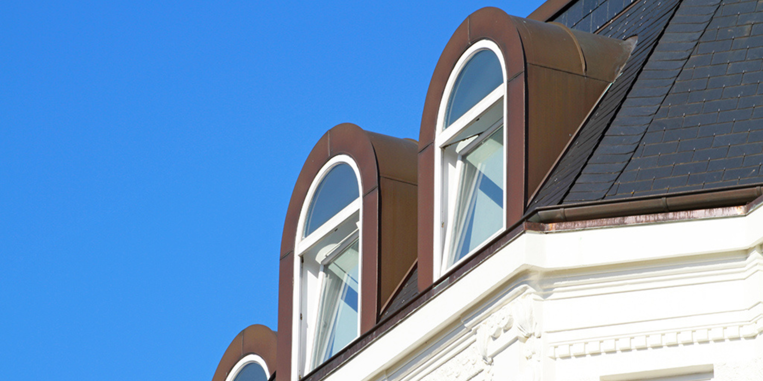 A barrel dormer with a rounded roofline and vertical arched window, framed by dark cladding on a historic-style building.