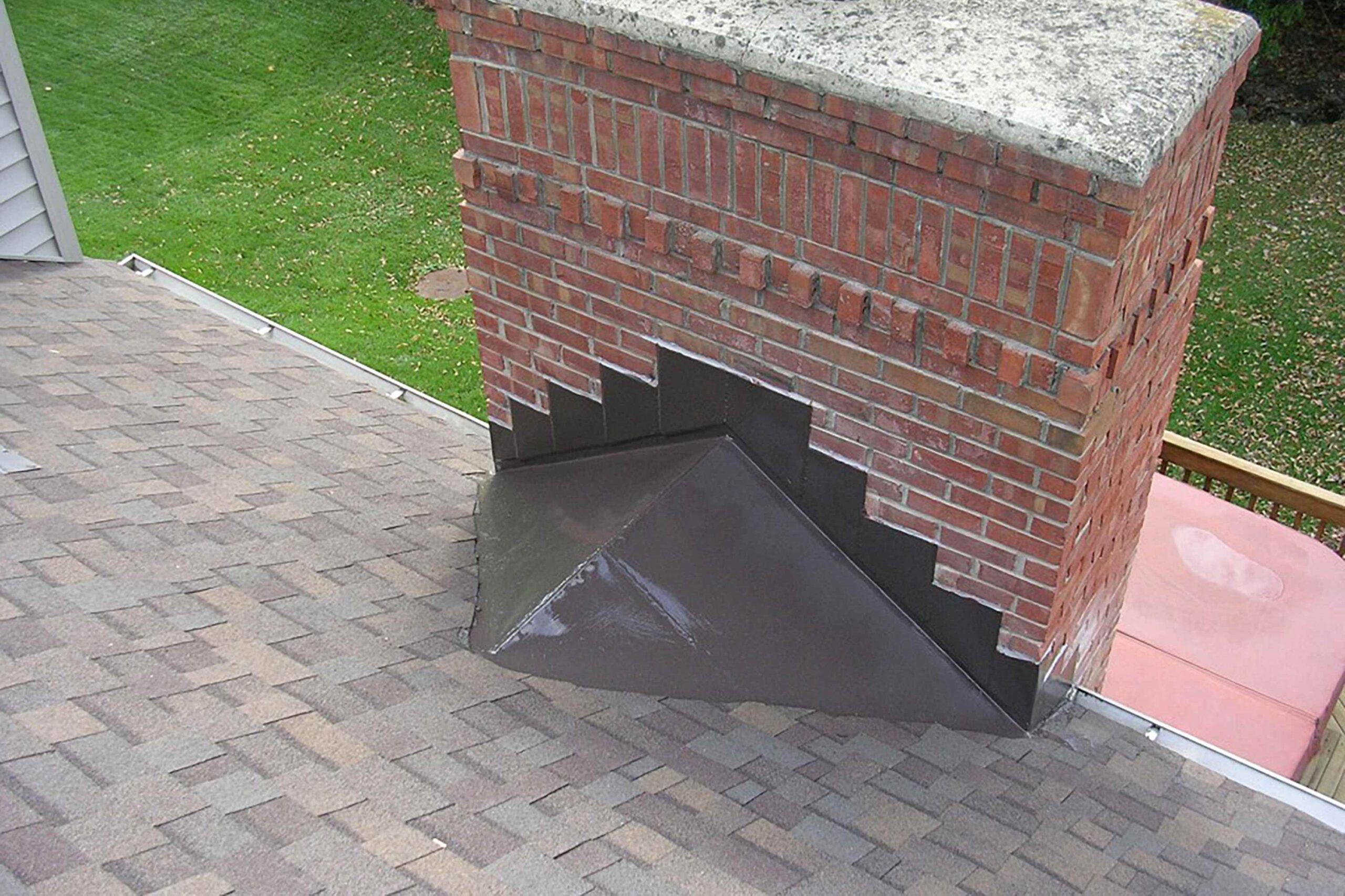 Stepped metal flashing on a brick chimney set into the mortar joints above a brown shingle roof