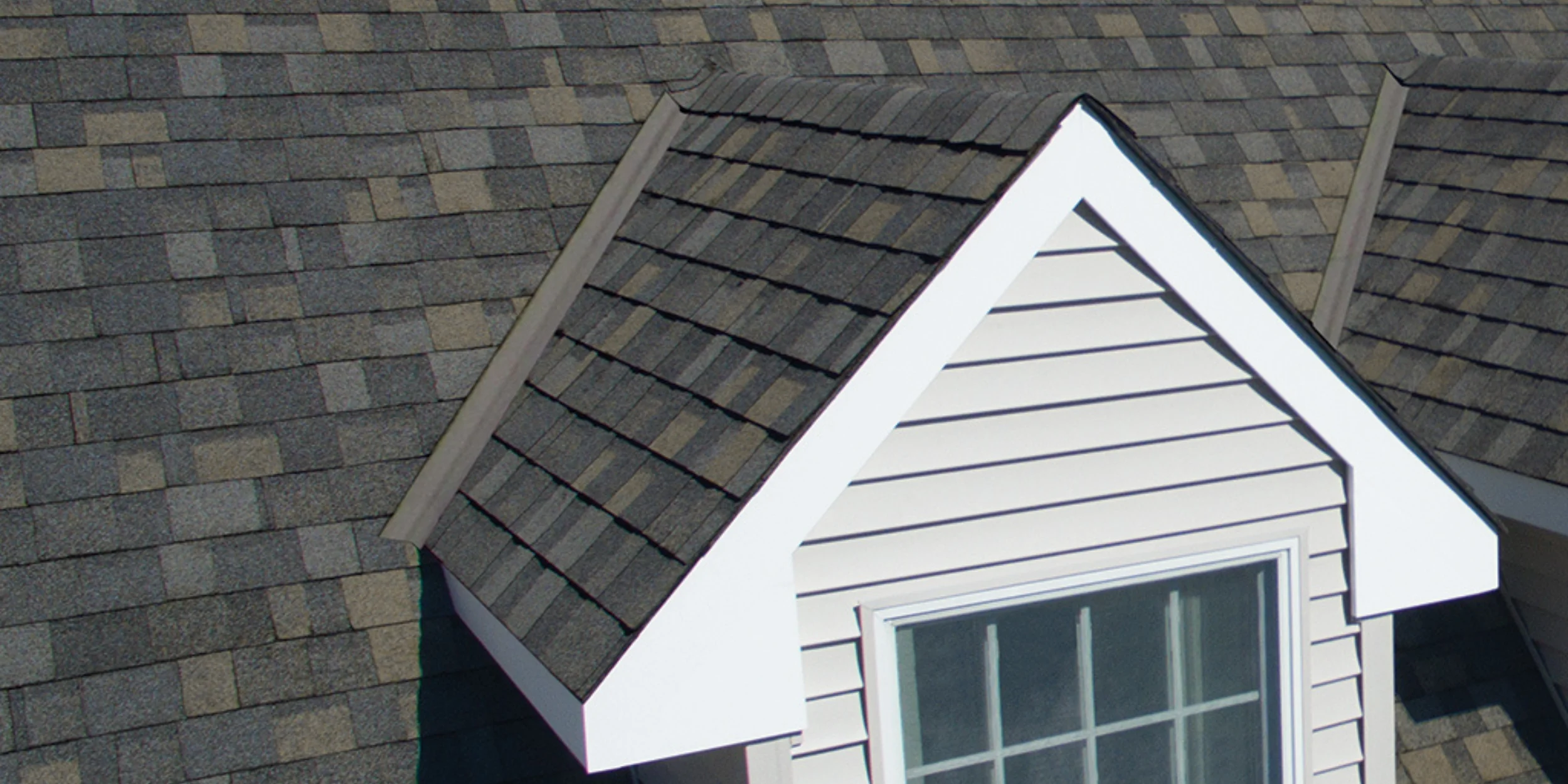 A finished gable dormer with white siding and trim, and architectural shingles that match the main roof.