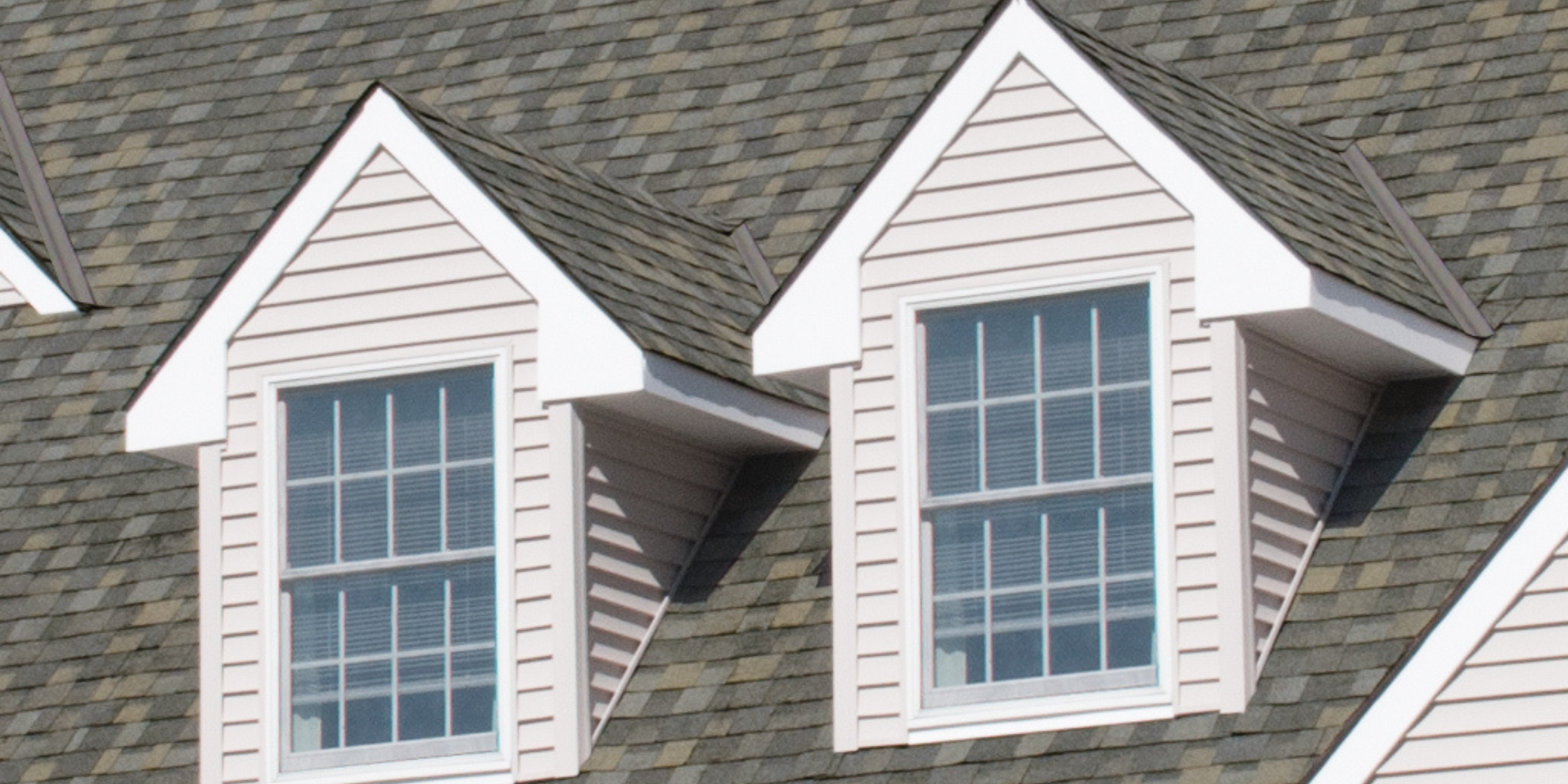 Twin gable dormers with steeply pitched roofs and white-trimmed vertical windows, projecting from a vinyl-sided upper story.