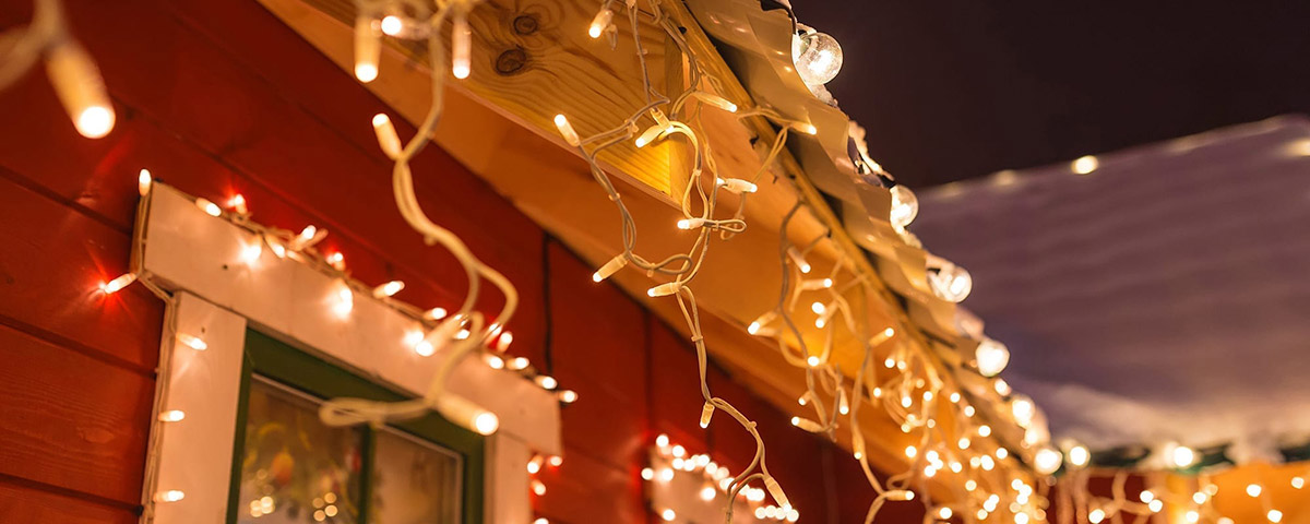 Warm white icicle lights hanging from the eaves and around the windows of a red house at night.