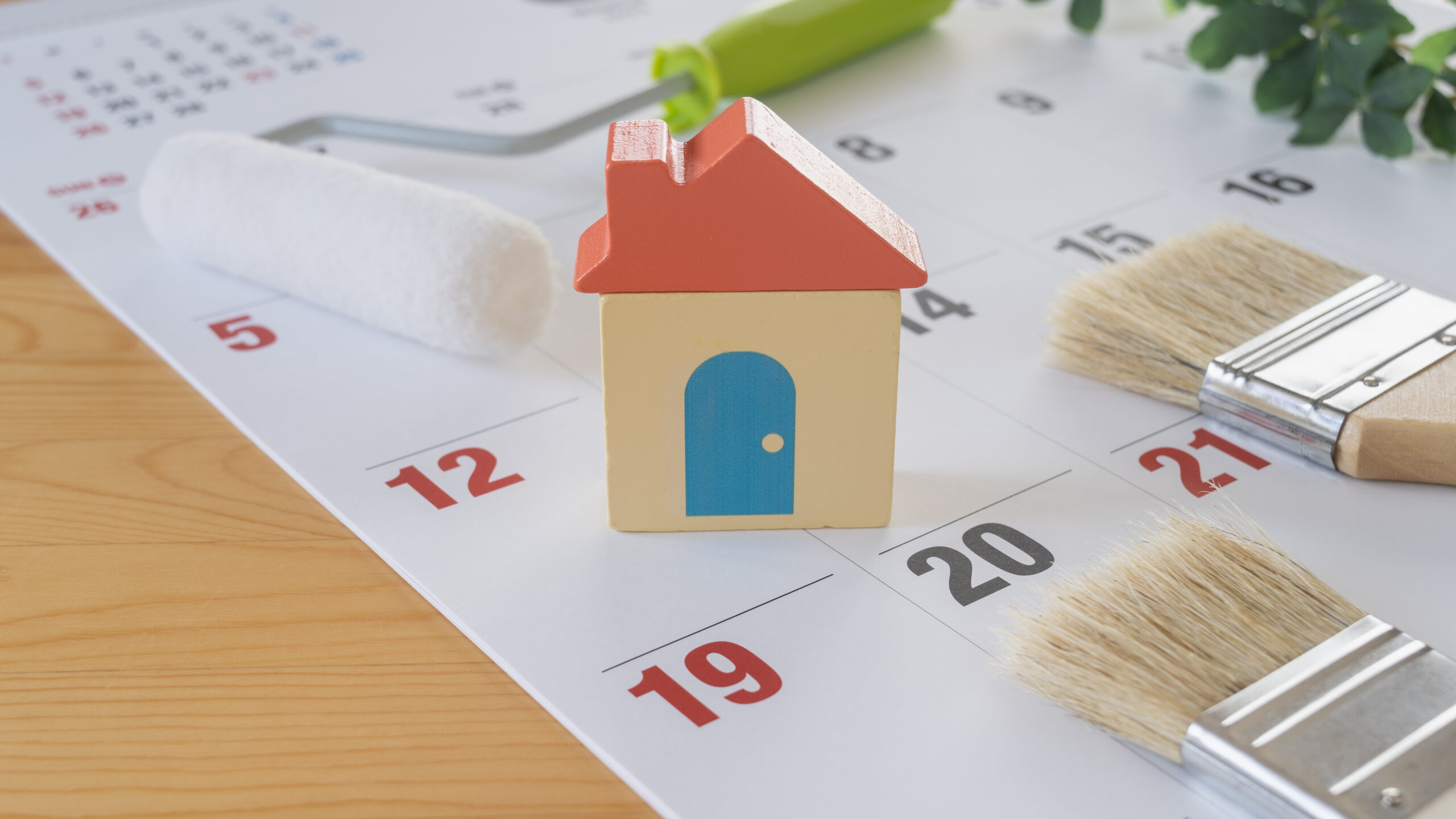 Small model house on a calendar with a paint roller and brushes, suggesting home project planning.