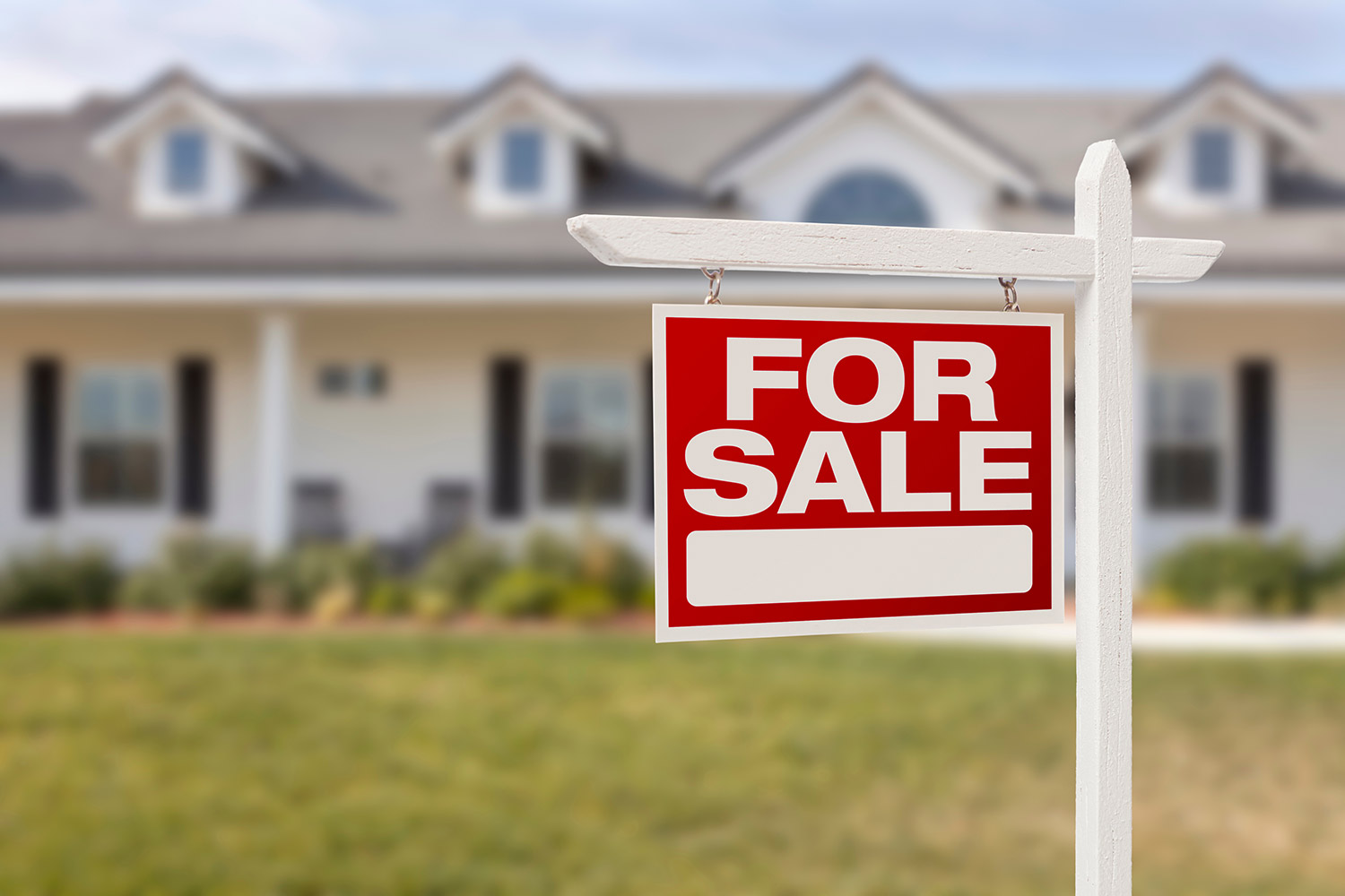 Red and white For Sale sign in front of a blurred house and lawn.