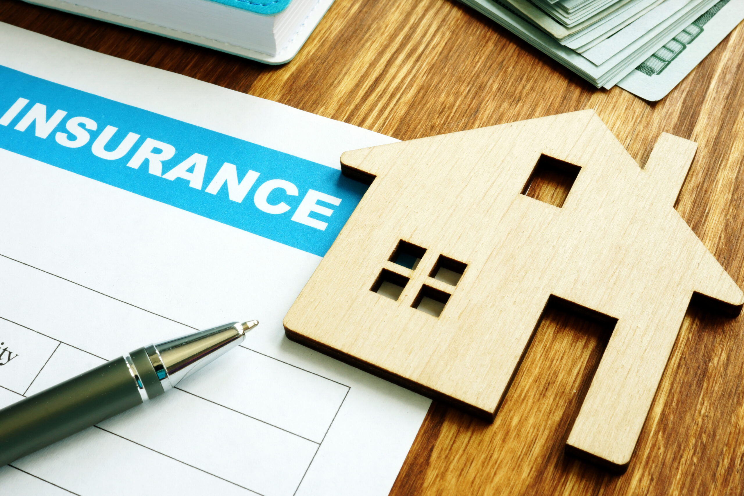 Insurance form with a wooden house cutout, pen and cash, representing homeowner roof insurance.