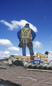roofer on top of roof with rolls of roofing material