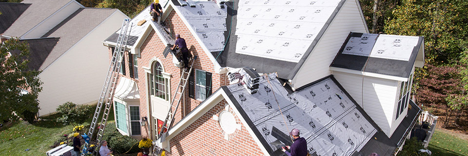 Aerial view of workers on ladders and a roof installing underlayment on a brick house