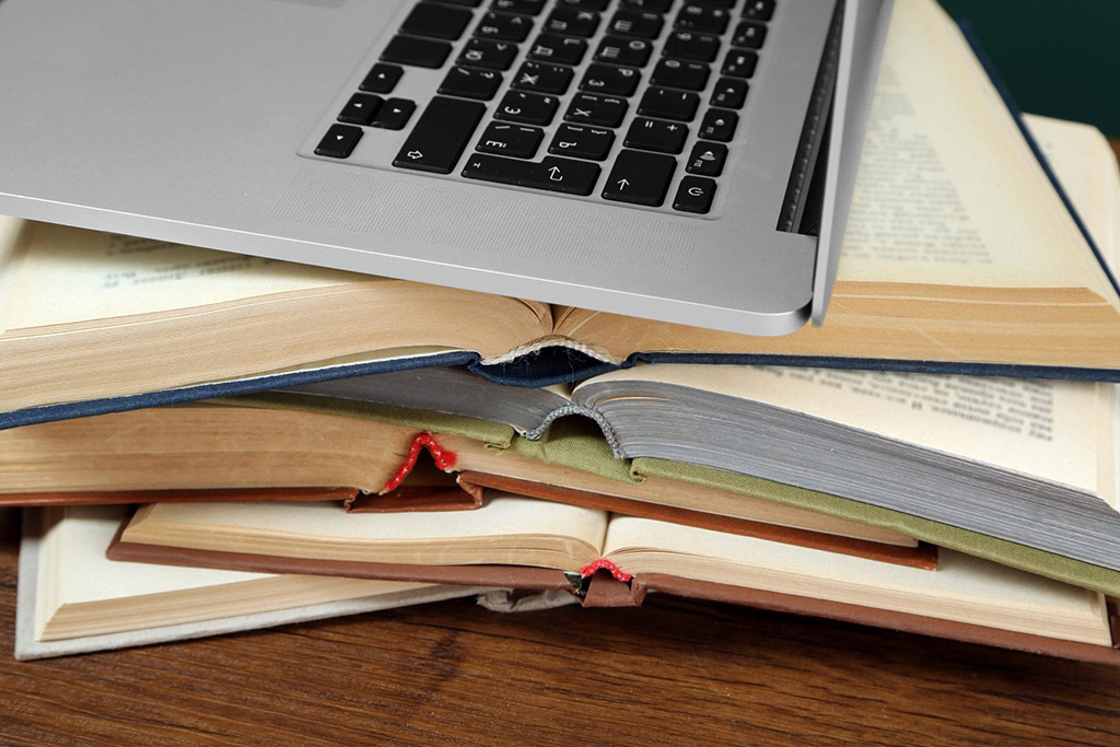 Laptop resting on a pile of open books on a wooden table