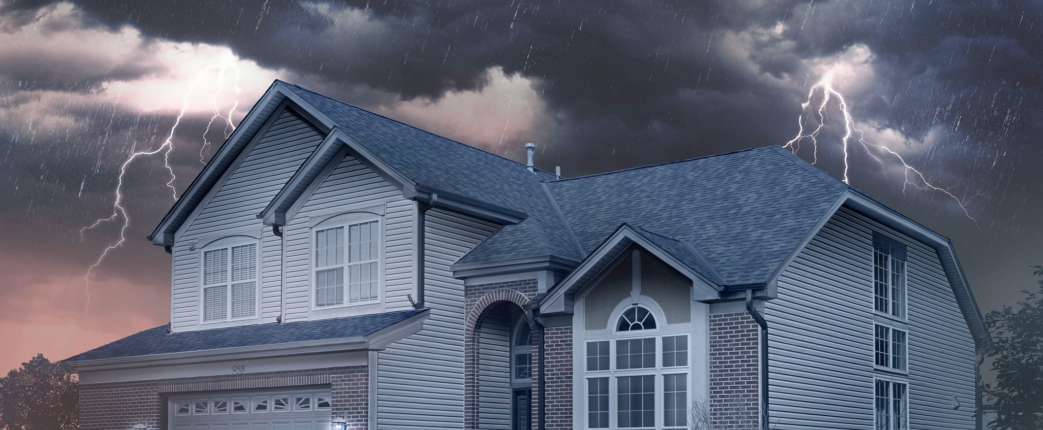 Storm clouds with lightning loom over a large home with an IKO roof.
