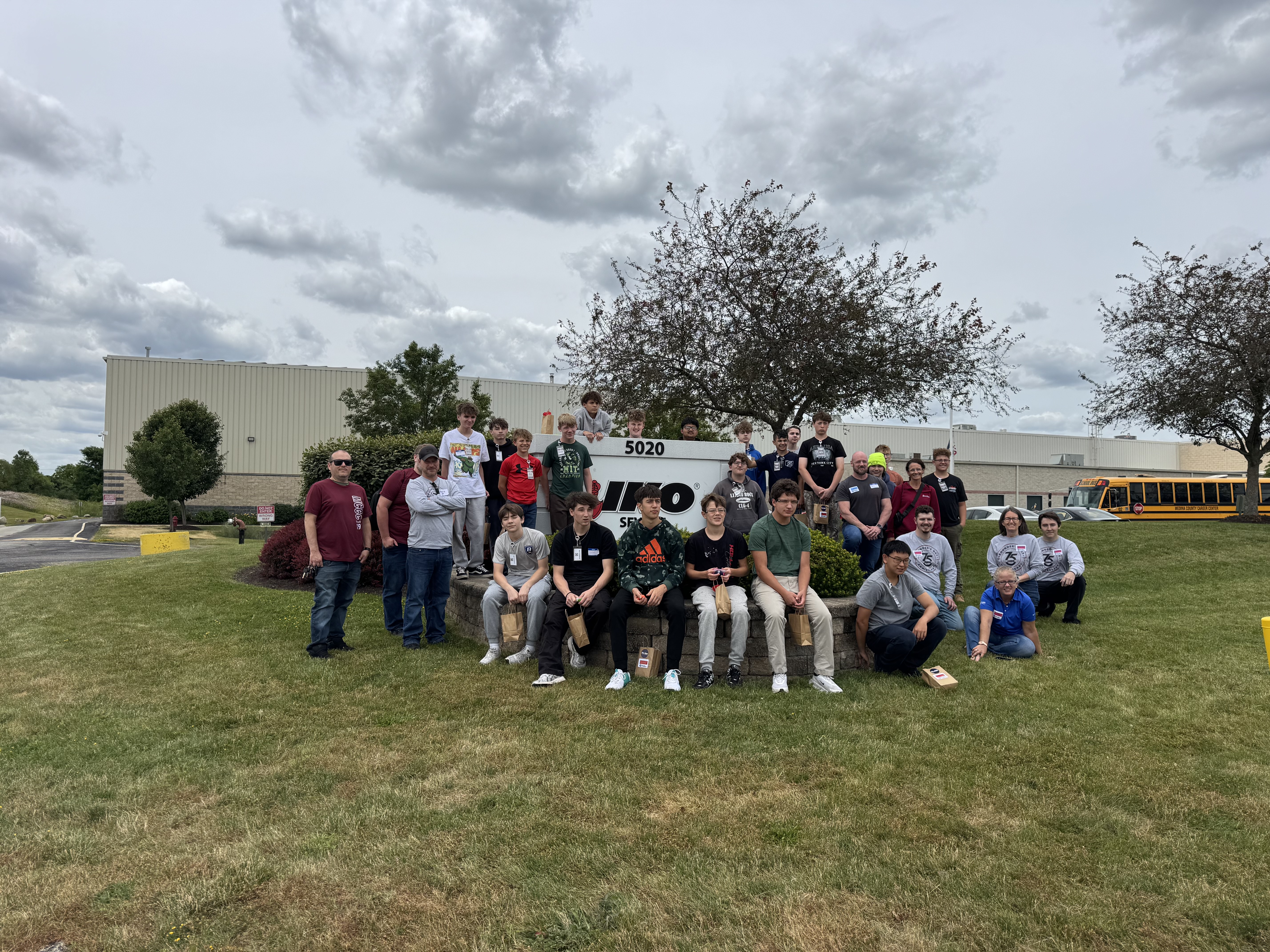 Un grand groupe d’étudiants et d’employés pose sur une pelouse devant un bâtiment IKO.