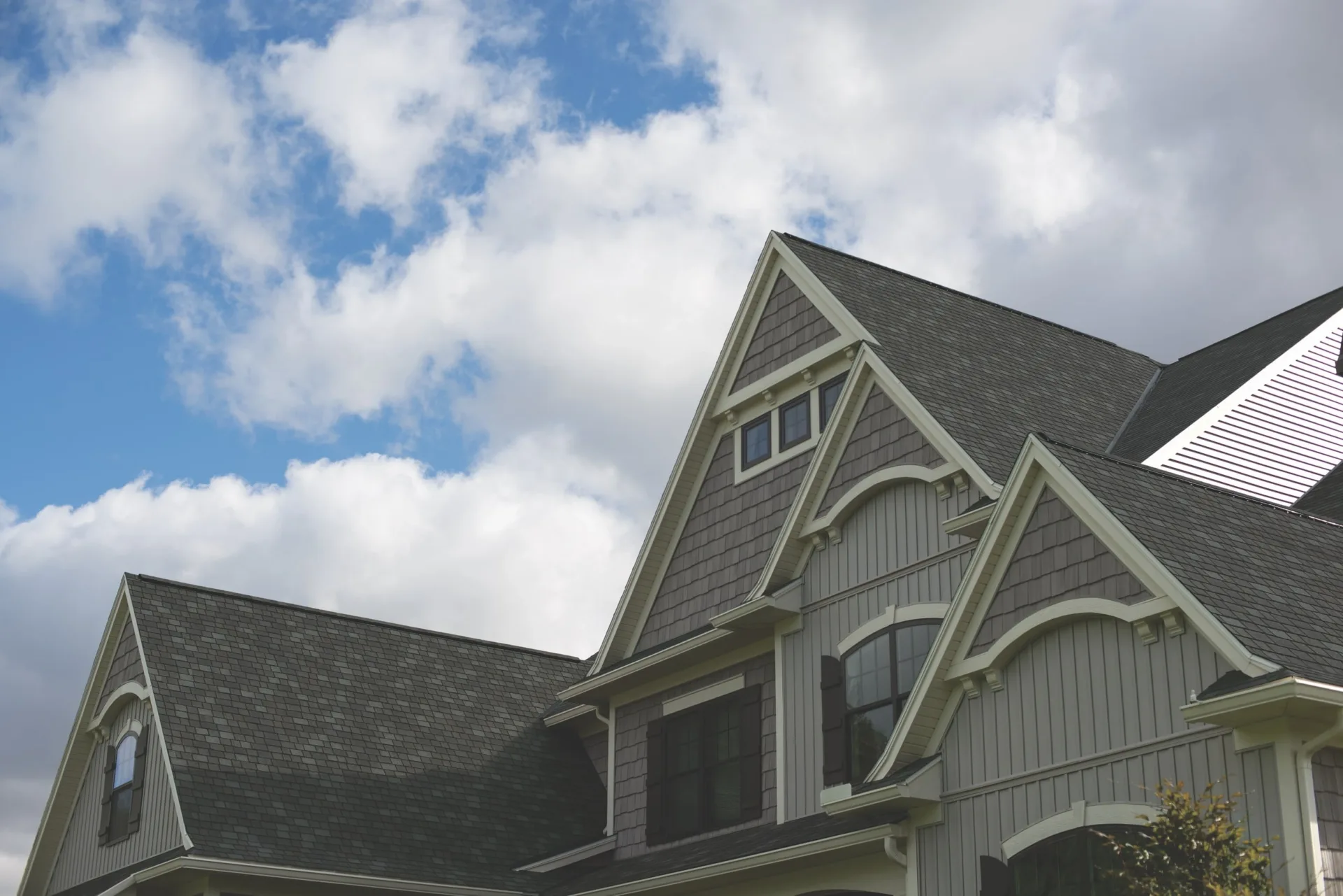 The gabled roof of the two-story house, clad in Mountain Slate shingles, features decorative woodwork and crisp white trim against a partly cloudy sky.