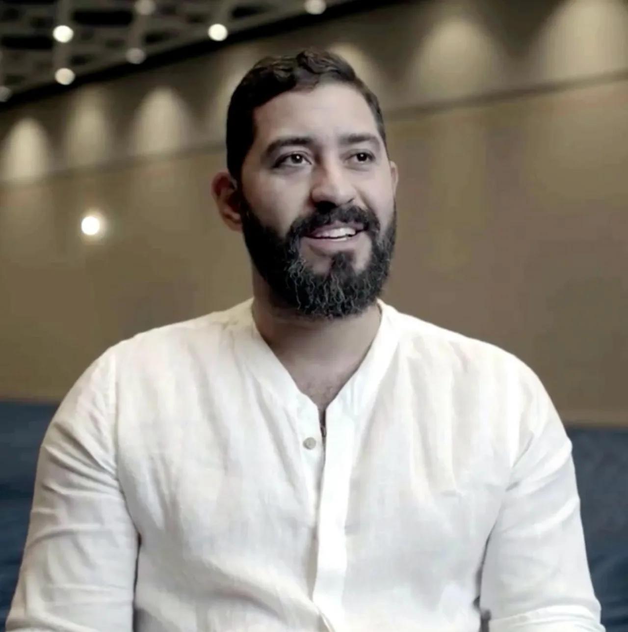 Homme barbu souriant en chemise blanche regardant hors caméra dans une salle d'événement