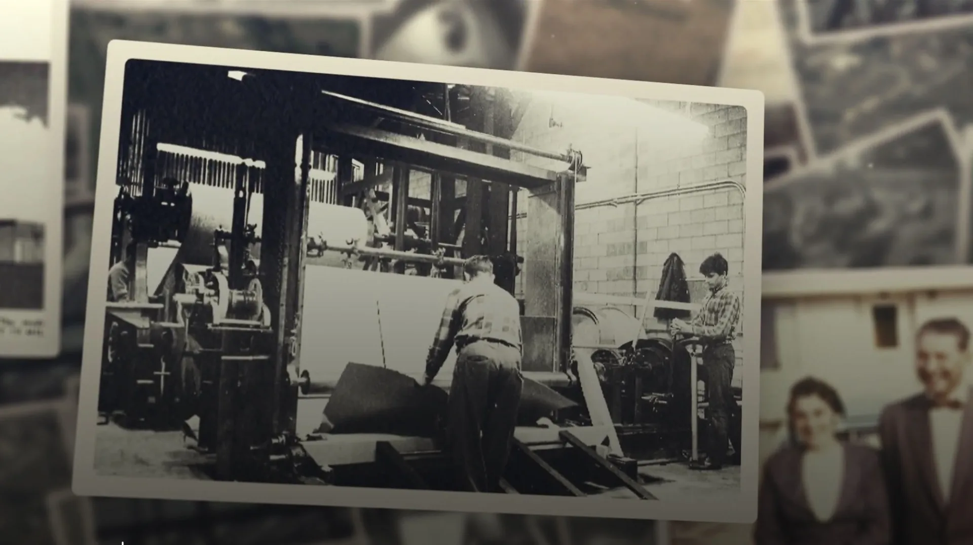 En esta fotografía en blanco y negro, trabajadores dedicados operan una gran máquina industrial en una fábrica de IKO. Dos hombres manejan materiales con gran concentración, mostrando la diferencia que aporta la mano de obra calificada en cada operación.