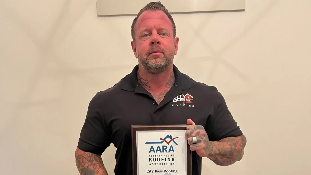 Una persona con tatuajes sostiene un certificado enmarcado de la Alberta Allied Roofing Association para City Boss Roofing, orgullosa de ser reconocida como miembro destacado de ROOFPRO.