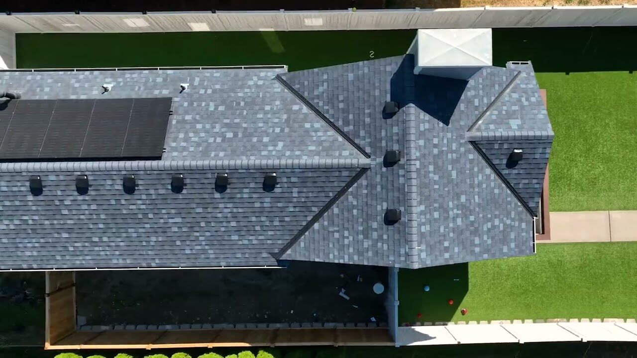 Una vista aérea muestra un edificio moderno con un techo gris oscuro de Dynasty Roofs y paneles solares eficientes, rodeado de céspedes verdes y un sendero sinuoso.