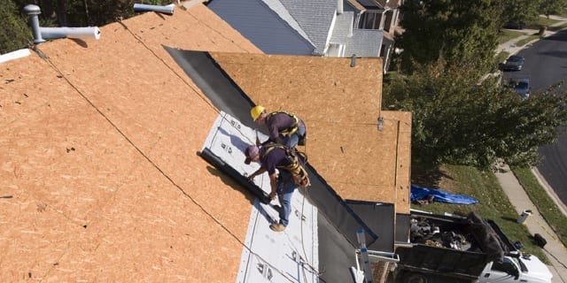 two roofers applying underlayment on a roof