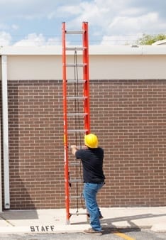 man setting ladder against a house in order to climb up the roof