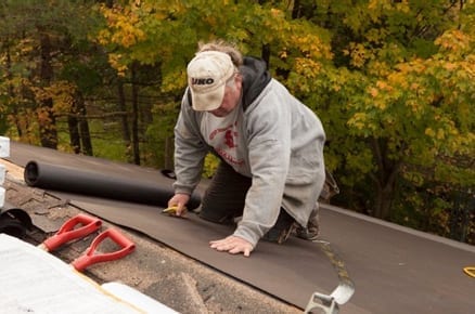 roofer laying out a roll of roofing felt on a steep slope roof