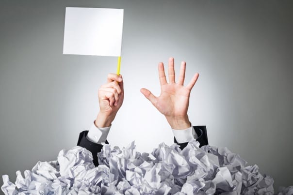 man buried under a pile of paper, waving a white flag