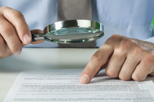 man using a magnifying glass to read the fine print on a roofing contract