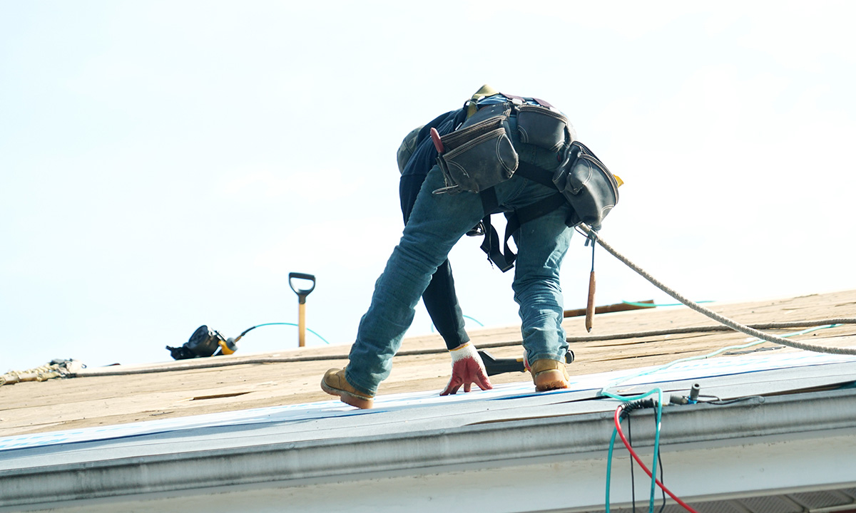 roofer installing underlayment with tools on a roof
