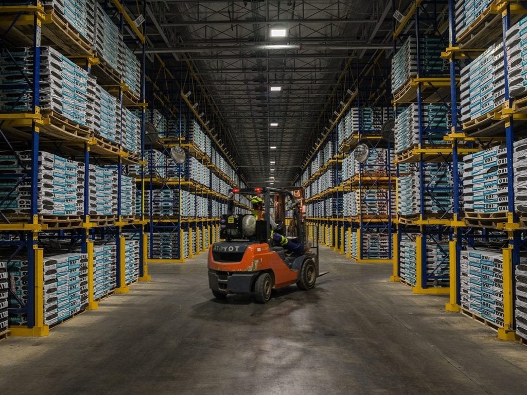 worker driving forklift in aisle of shingle storage warehouse