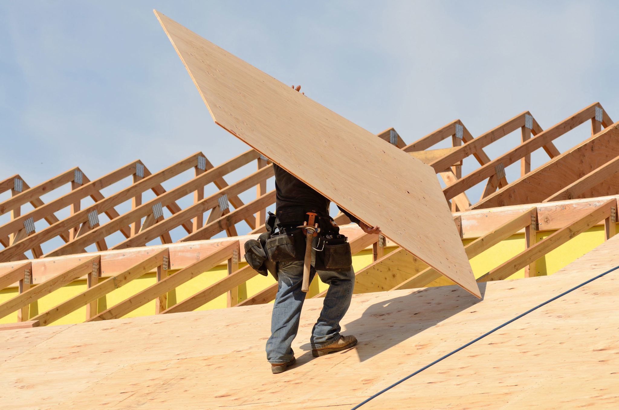 travailleur transportant un panneau de contreplaqué sur un toit en pente en construction