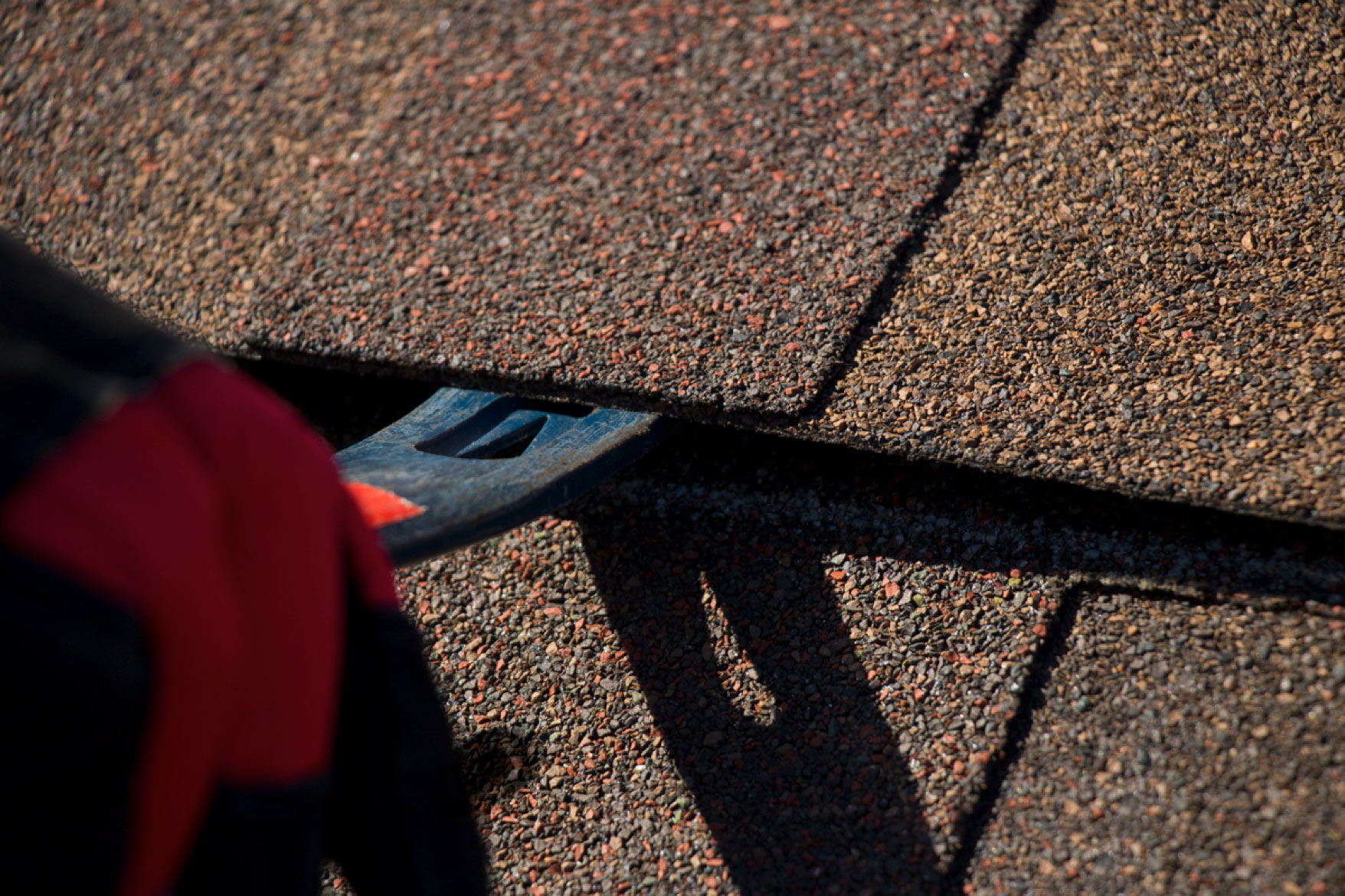 close view of a pry bar being used to lift a shingle