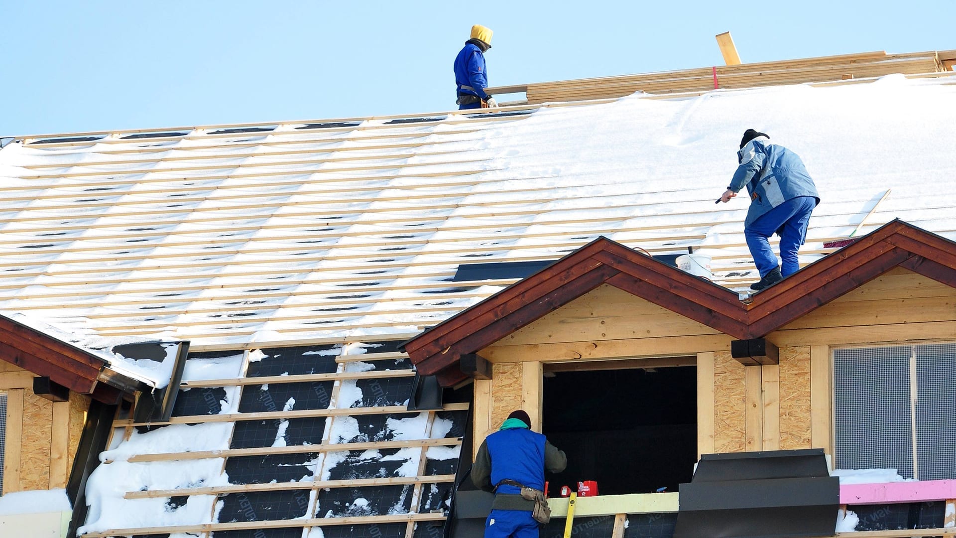 workers on a snow-covered strapped roof deck