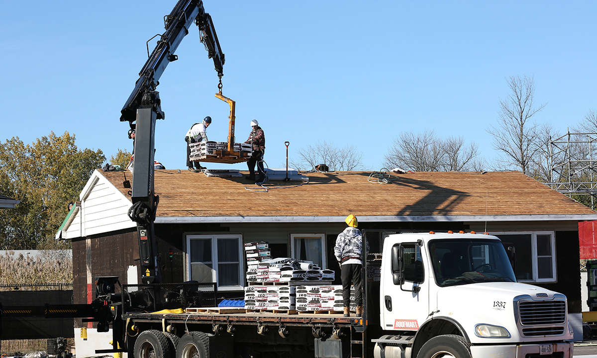 Boom truck lifting shingles to the top of a roof