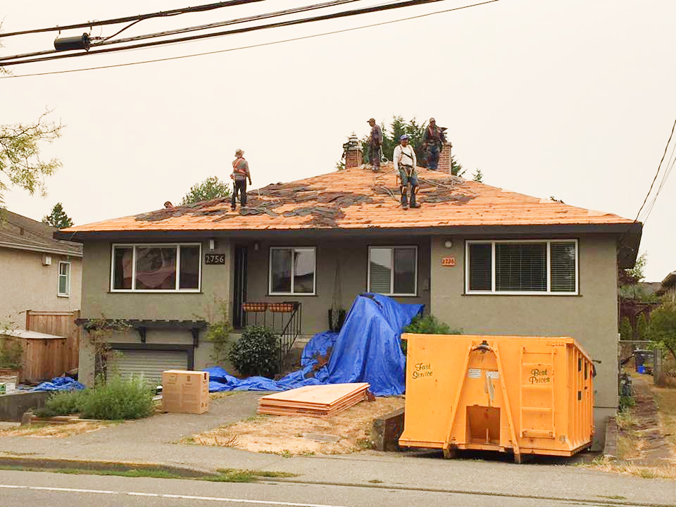 roofers removing shingles from roof and into dumpster
