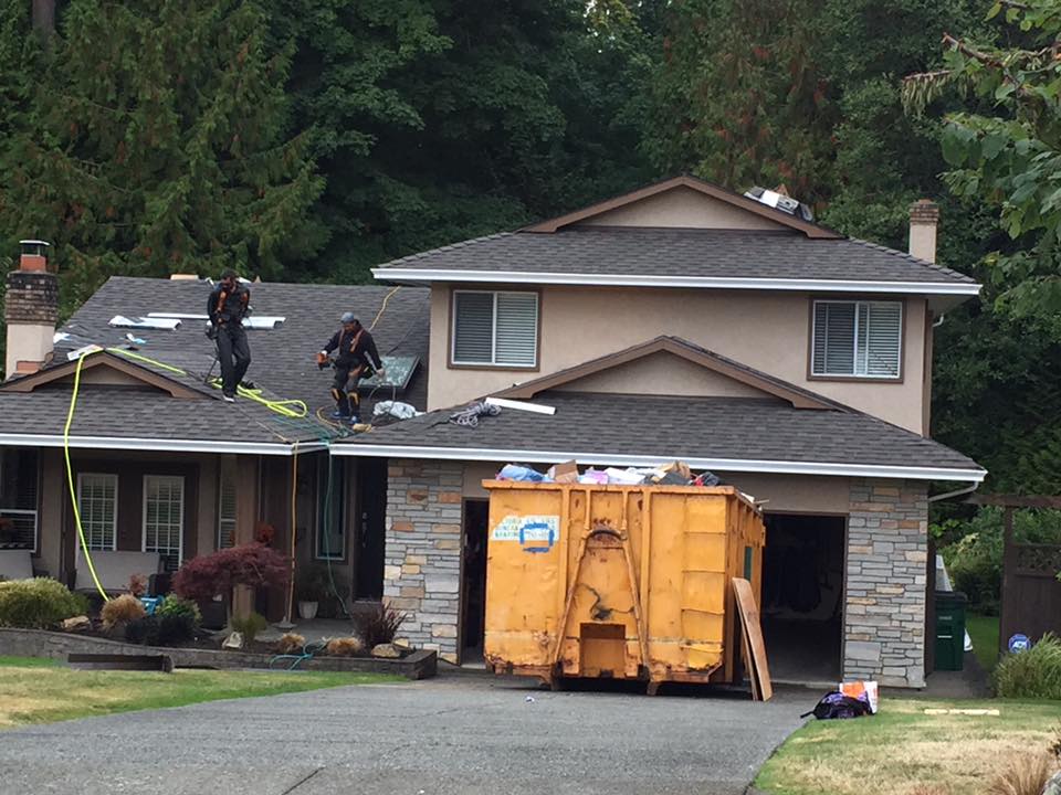 dumpster placed on driveway as roofers complete shingle roof