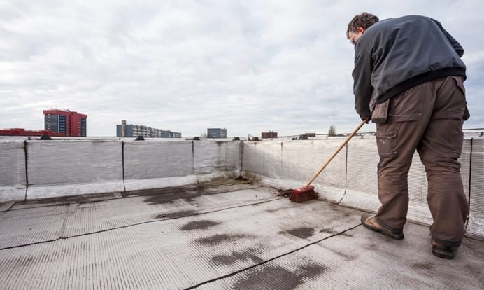 Man cleaning debris off of a flat roof with a broom.