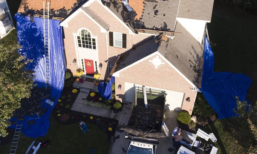 An aerial view of a home with tarps placed over landscaping during a roof replacement.