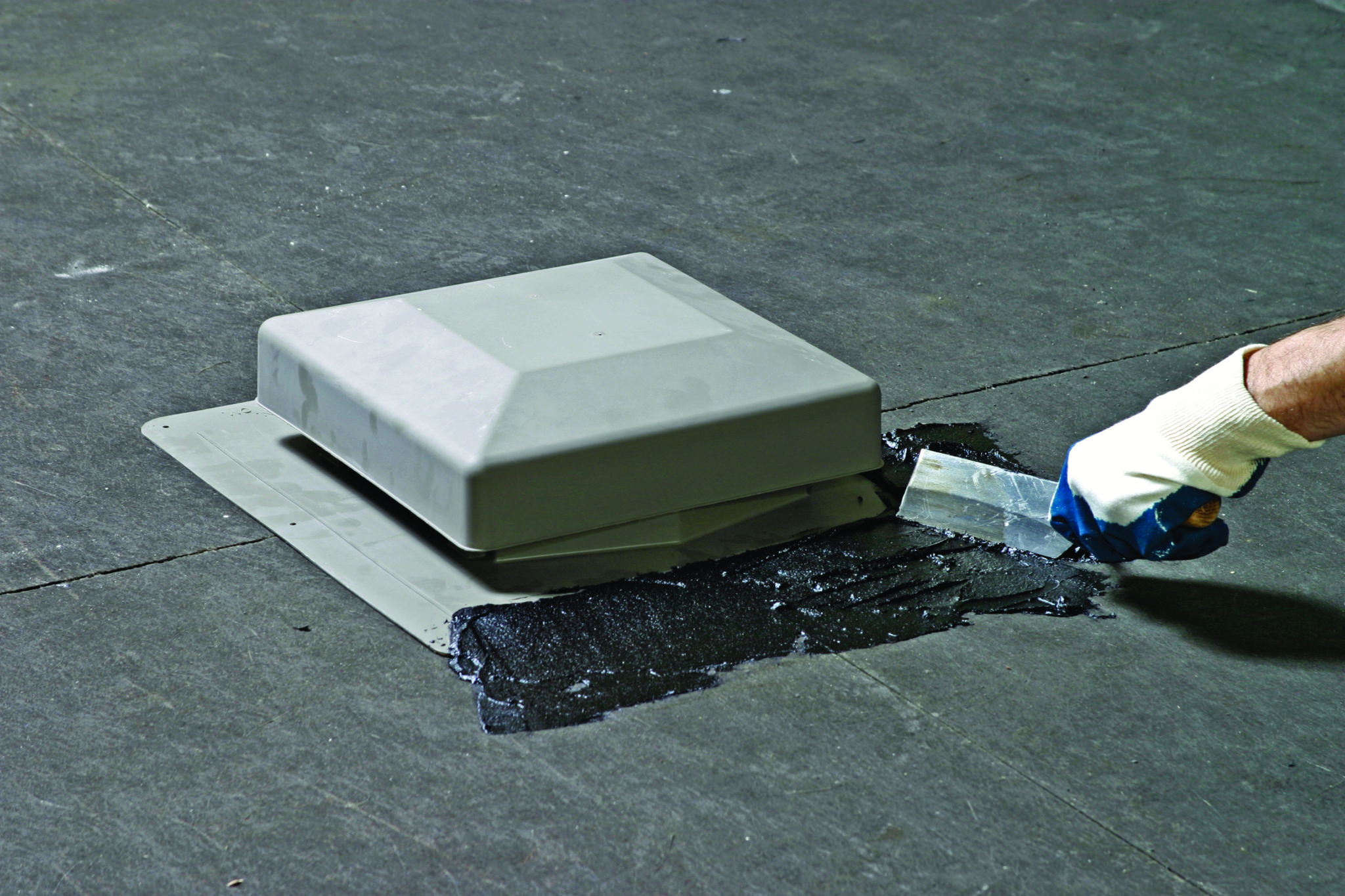 roofer applying roofing cement with a trowel to seal a static roof vent